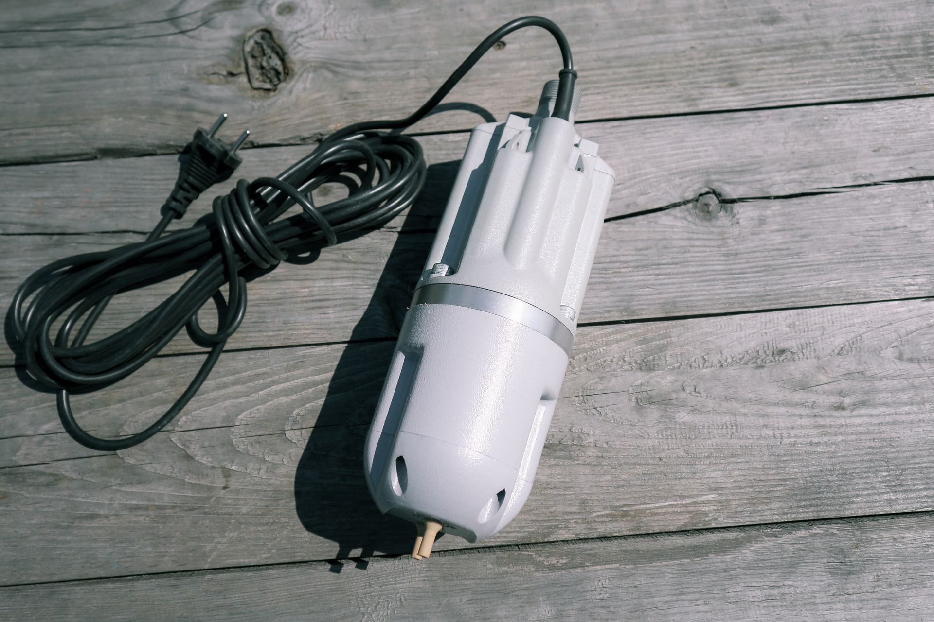 A white object with a black cord attached to it is sitting on a wooden surface.