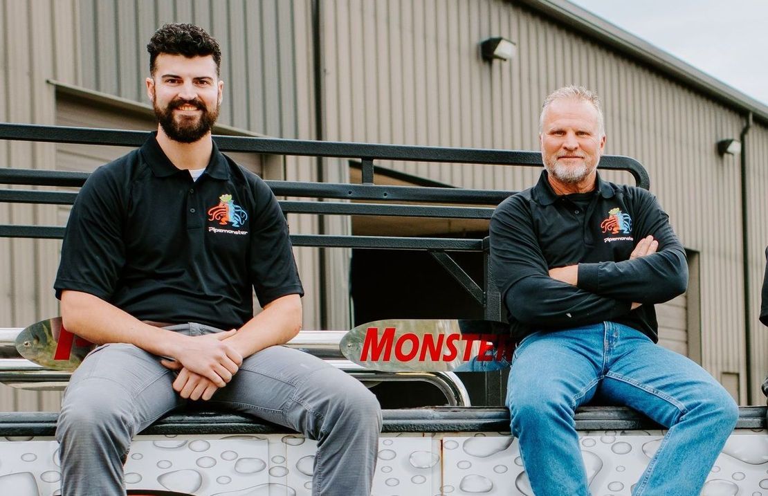 Two men are sitting on the back of a truck.