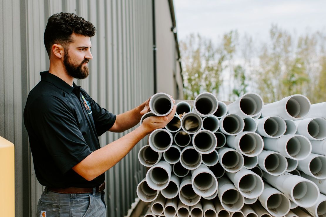 A man is standing next to a pile of pipes.