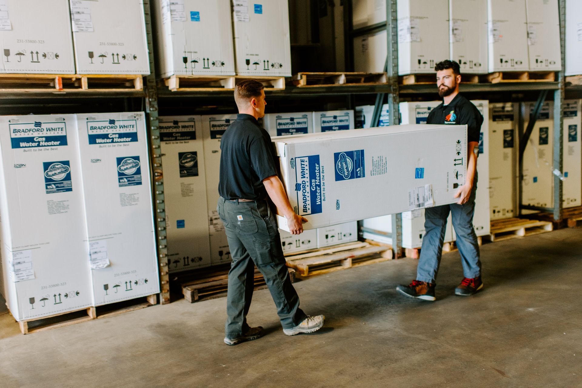 Two men are carrying a large box in a warehouse.