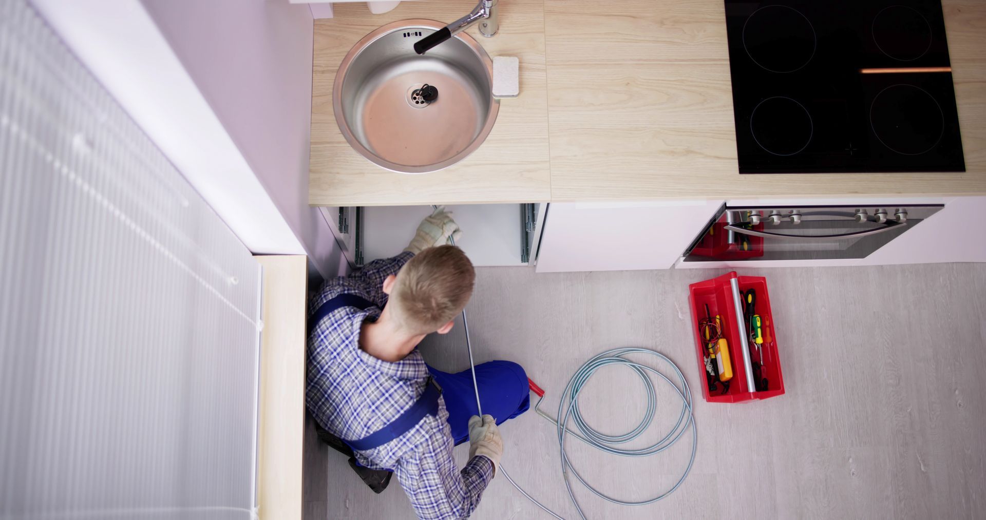 A plumber is fixing a sink in a kitchen.