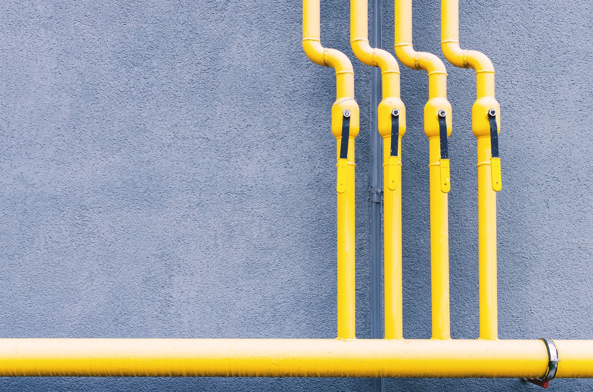A row of yellow pipes are lined up against a gray wall.