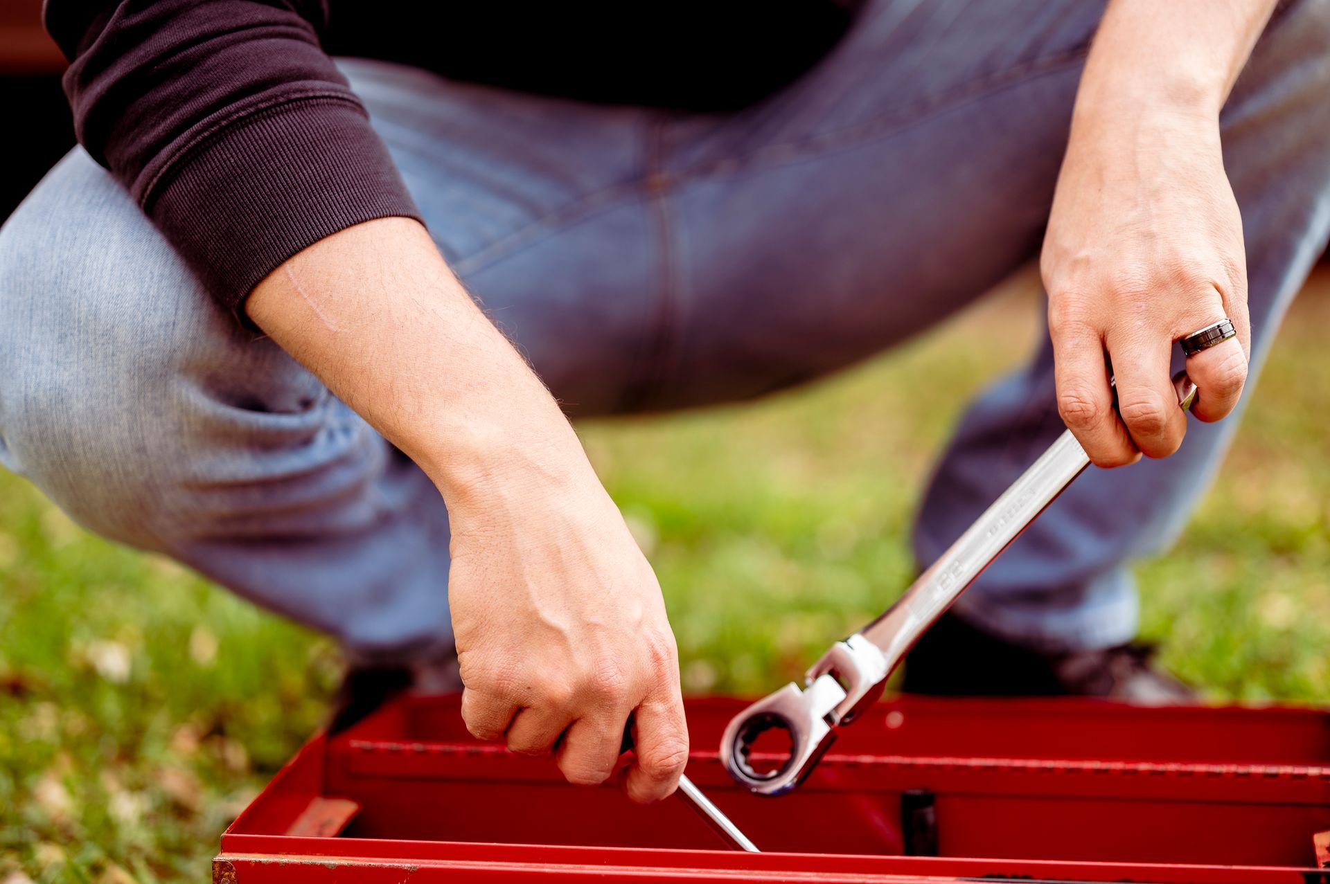 A man is kneeling down holding a wrench and a screwdriver.