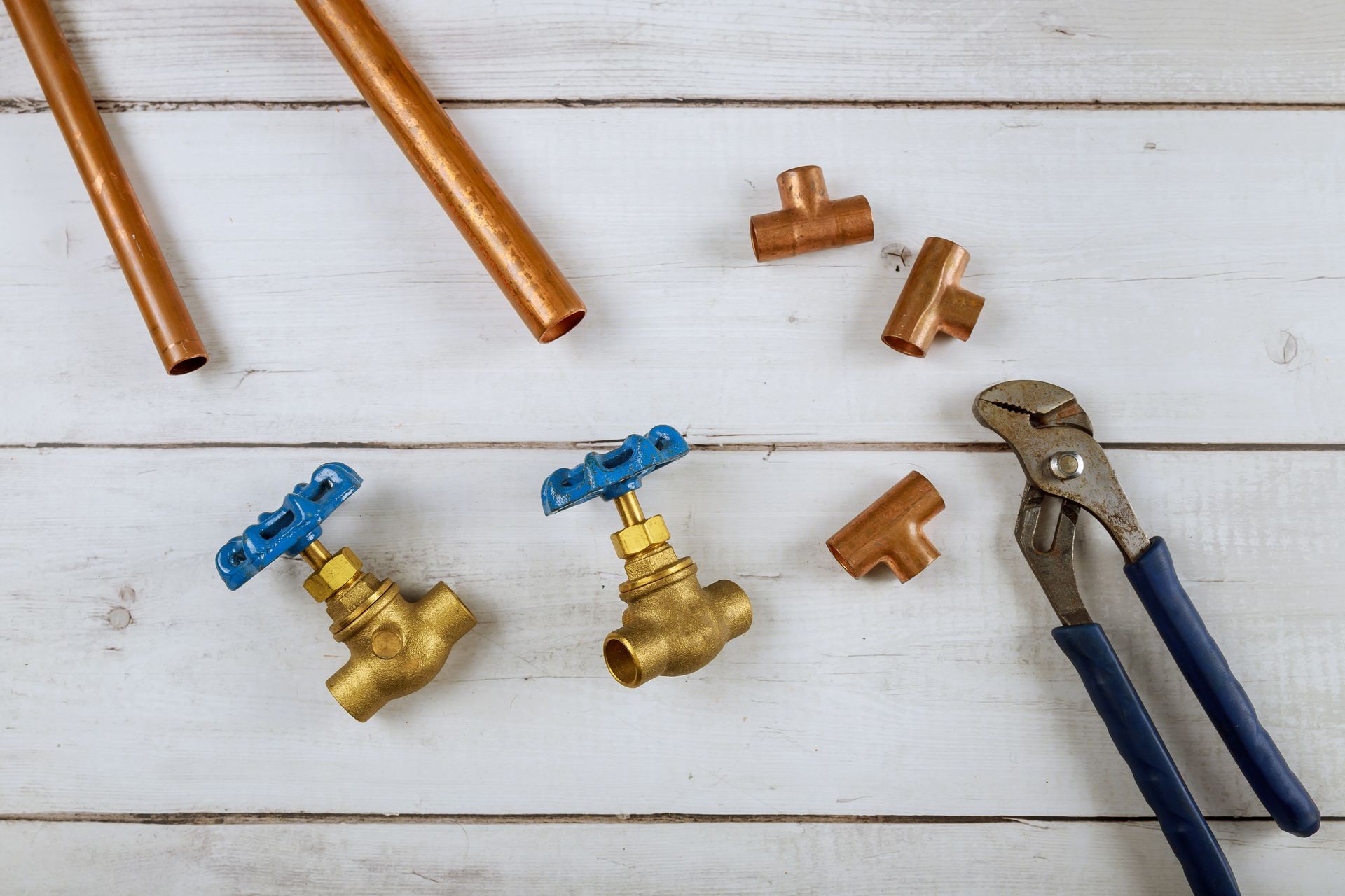 Copper pipes , valves , and pliers on a wooden table.