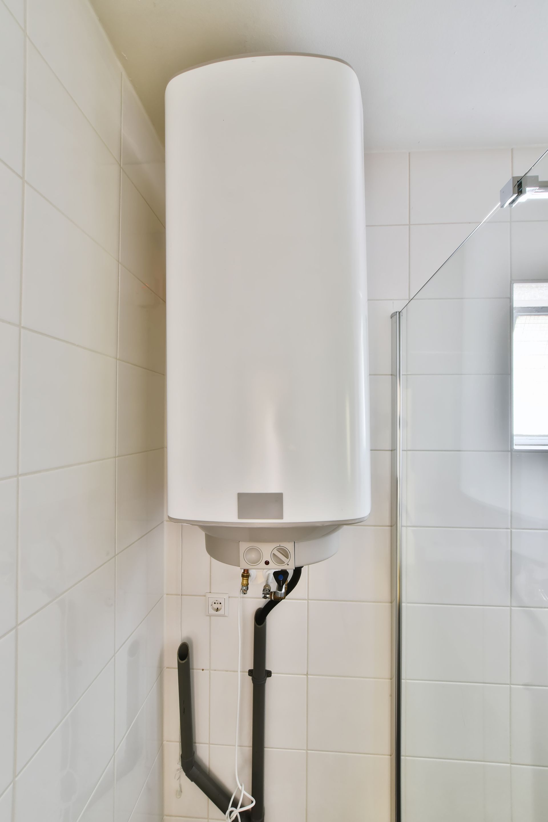 A white water heater is hanging from the ceiling in a bathroom.