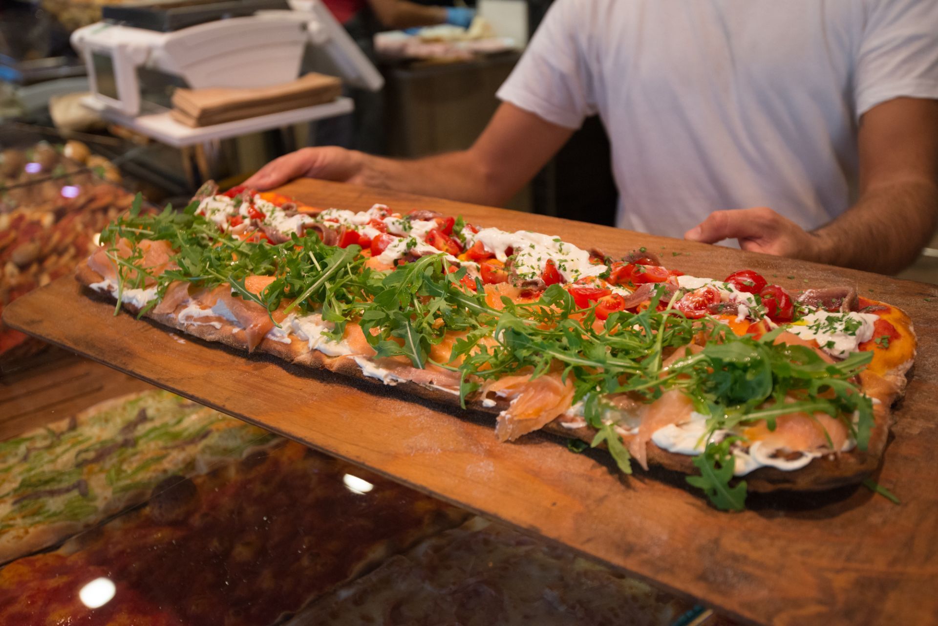 Un uomo tiene in mano una lunga pizza su un tagliere di legno.