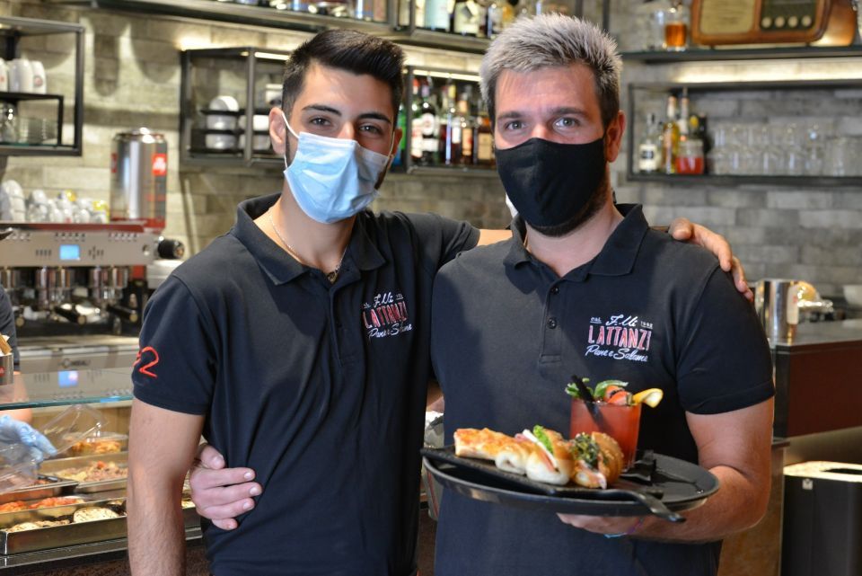 Due uomini che indossano maschere sono in piedi uno accanto all'altro e tengono in mano un piatto di cibo.