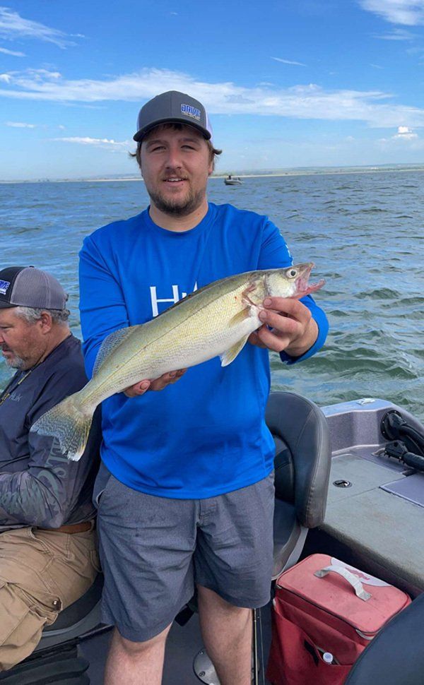 man in baseball cap and blue shirt holding fish