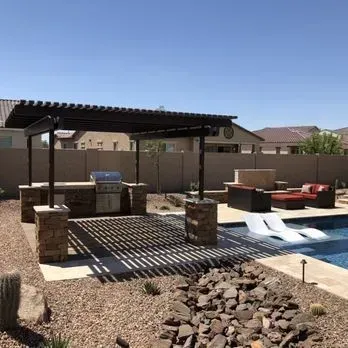 Outdoor kitchen and seating area by a pool under a pergola.