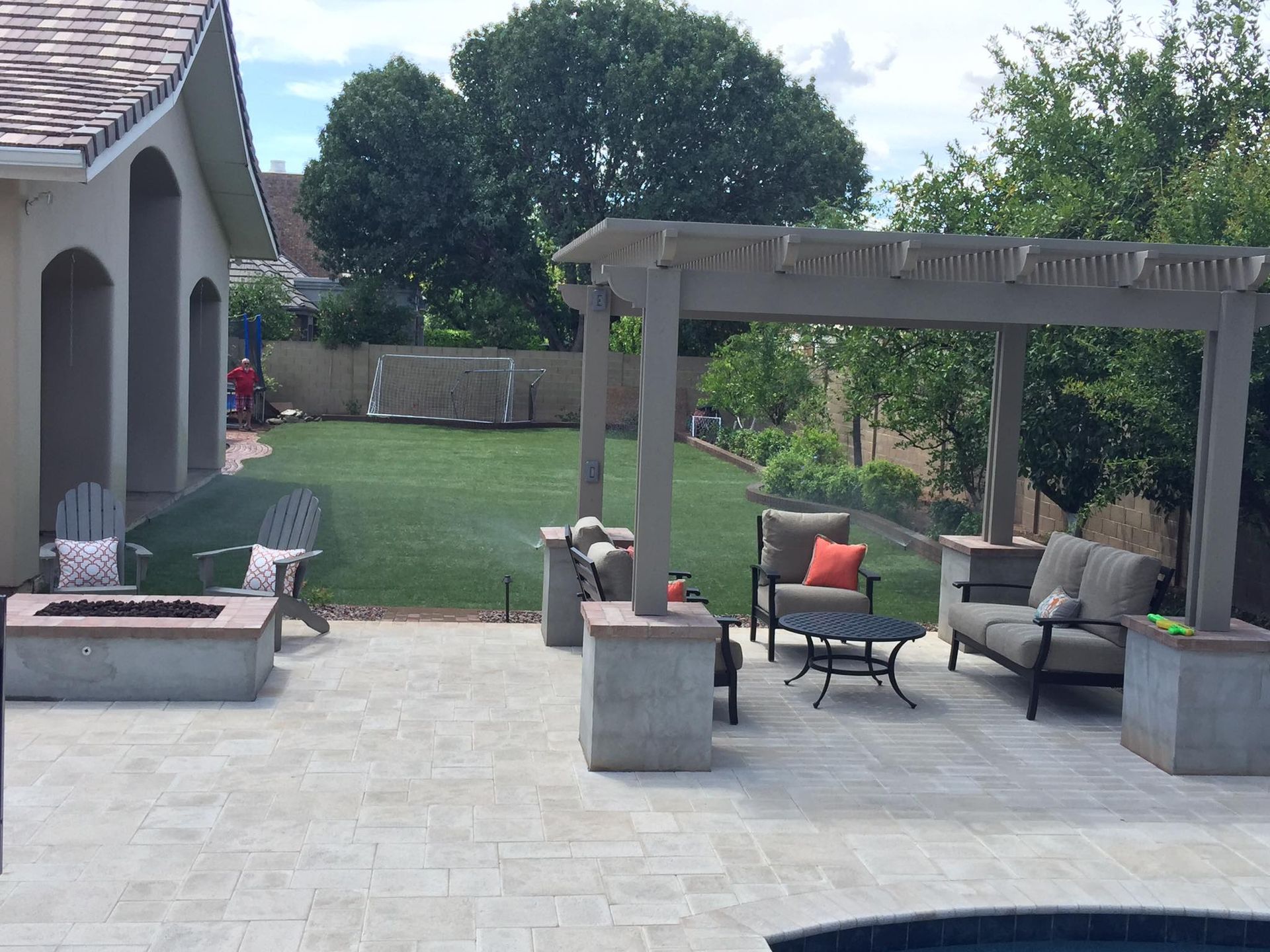 Outdoor patio with seating, fire pit, pergola, and lush green lawn.