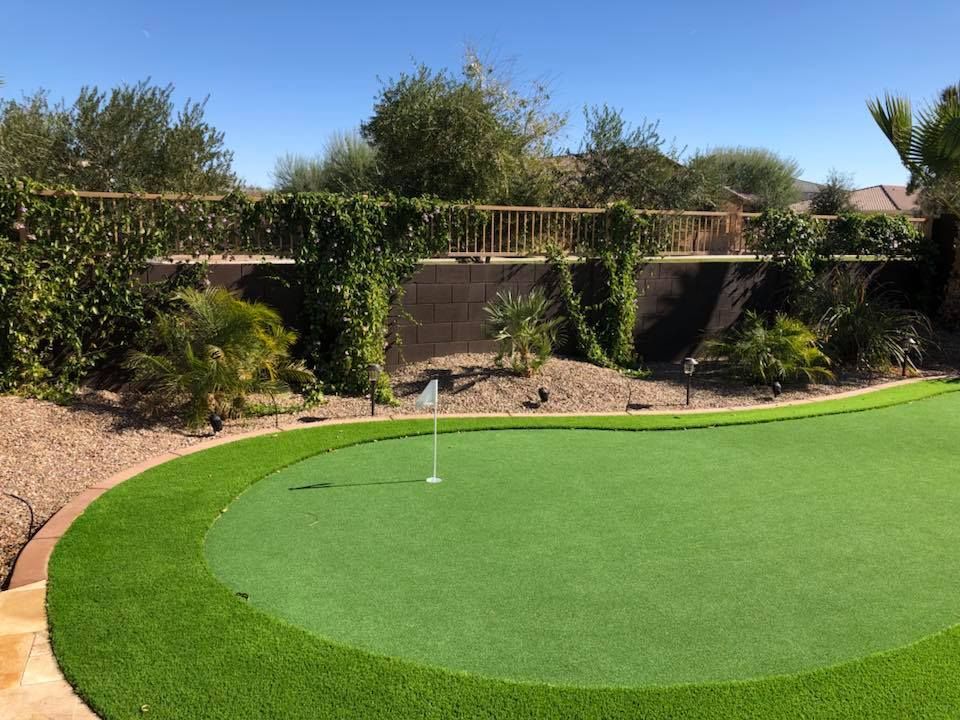 Artificial turf putting green in a backyard, with a flag and retaining wall lined with vines.