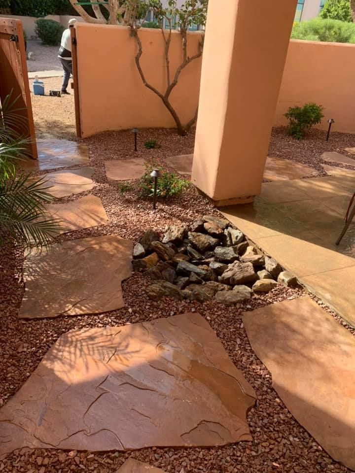 Flagstone path through a xeriscape garden with red gravel, small waterfall, and a stucco wall.
