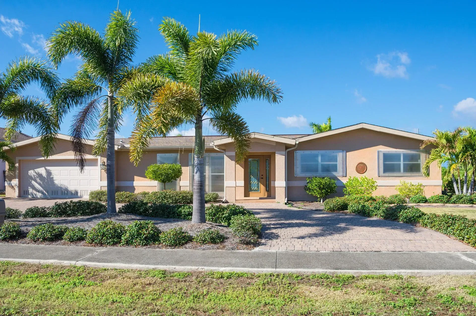 Tan ranch house with palm trees, blue sky, and green lawn.