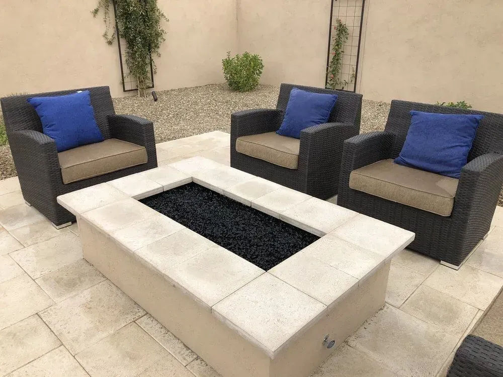 Outdoor seating area with three wicker armchairs, blue pillows, and a rectangular fire pit.