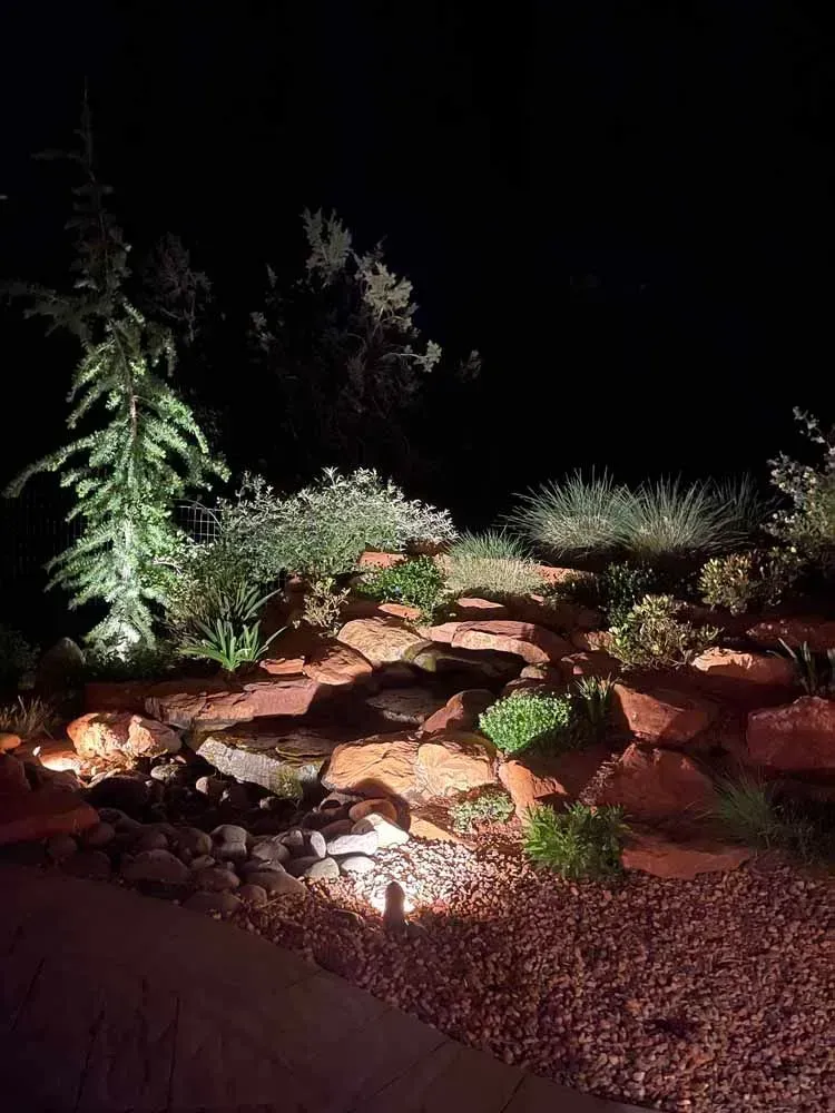 Nighttime landscape: red rock steps with illuminated plants and trees.