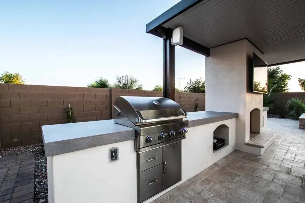 Outdoor kitchen with built-in stainless steel grill, counter, and covered seating area, against a brick wall.
