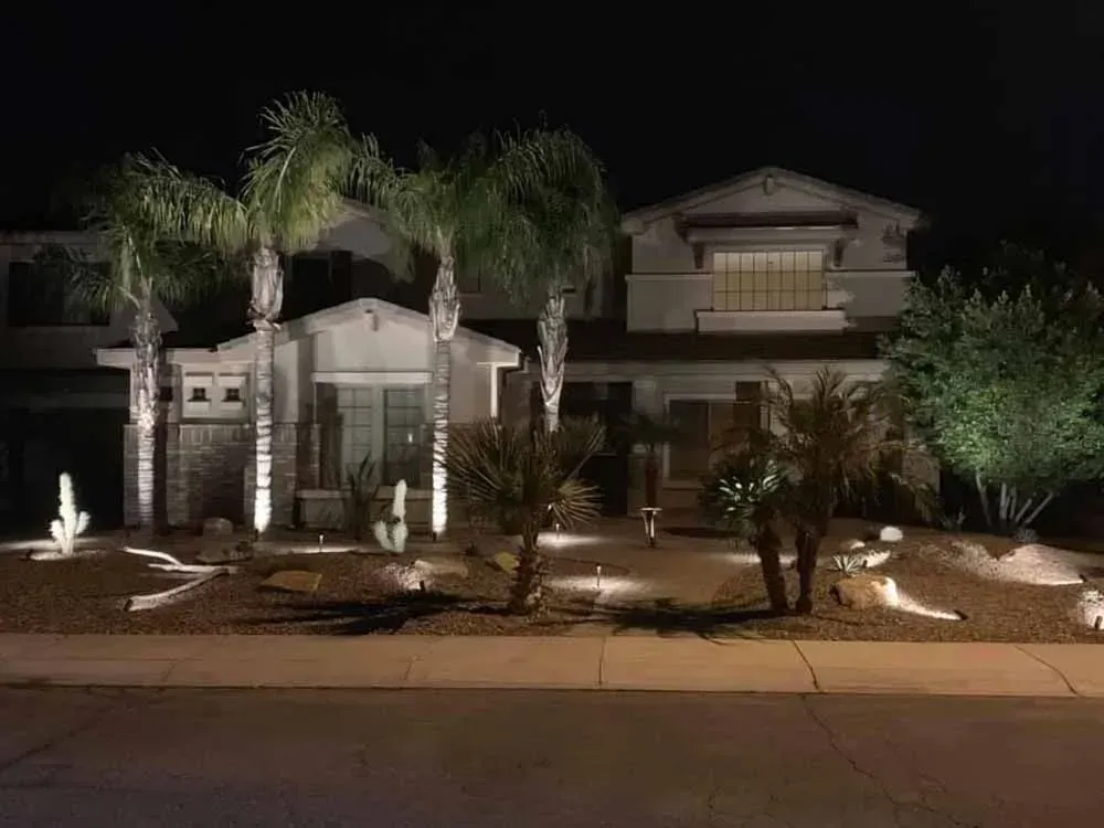 House exterior illuminated at night, featuring palm trees and desert landscaping.