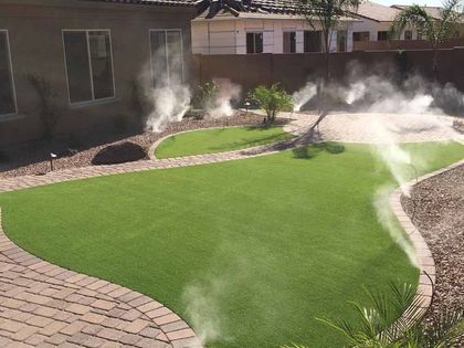 Lawn with misting system in a backyard; green grass, stone path, and shrubs.