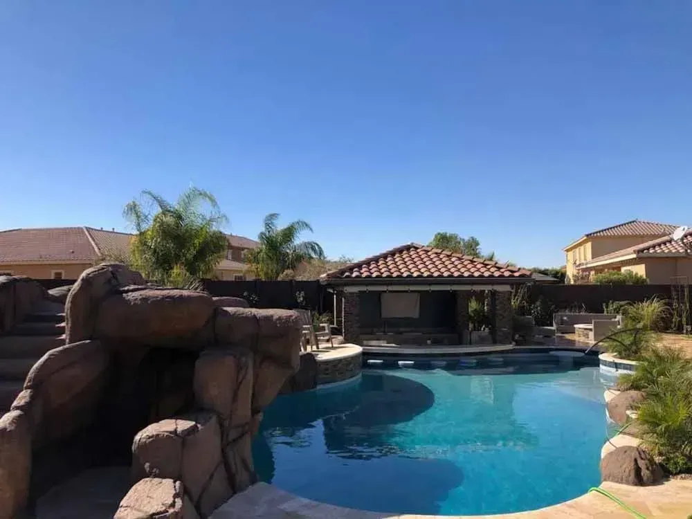 Backyard pool with rock features, swim-up bar, and blue sky.