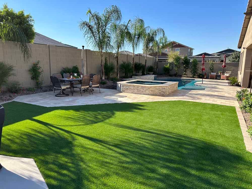 Backyard with pool, hot tub, dining area, and artificial grass under a sunny sky.