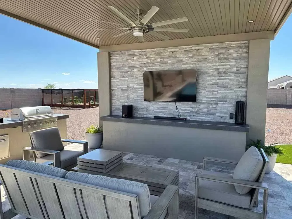Outdoor patio with a TV, speakers, seating, and grill under a covered structure.