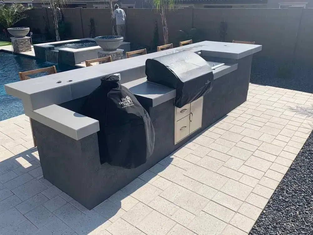 Outdoor kitchen with grill, covered smoker, and countertop; near a pool.