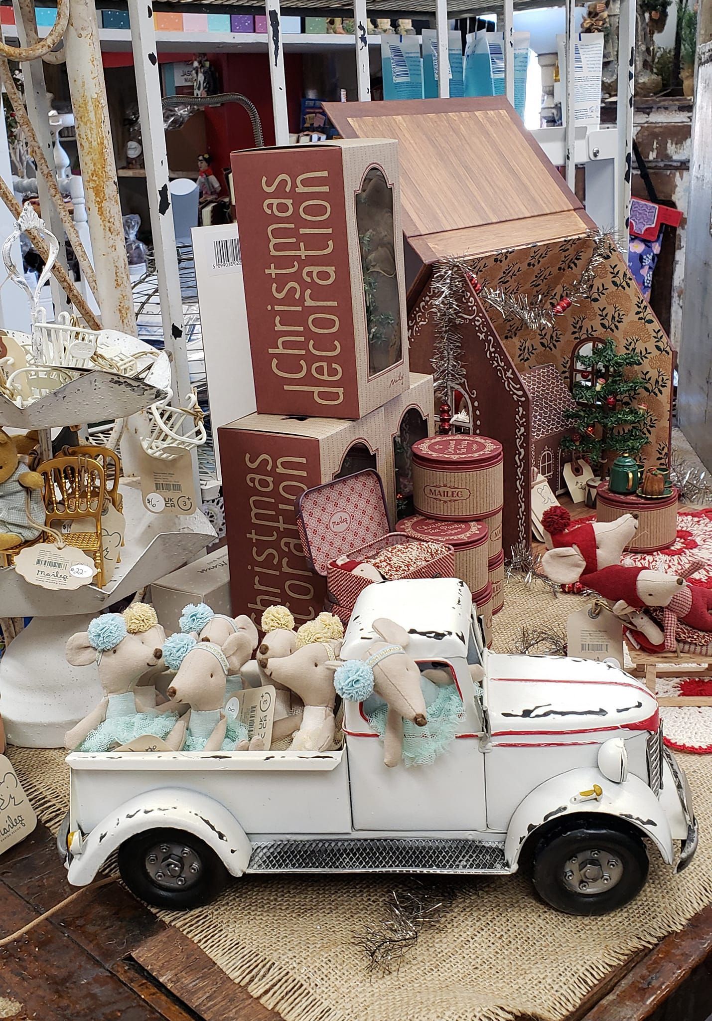 A white truck with teddy bears in the back is sitting on a table next to a gingerbread house.