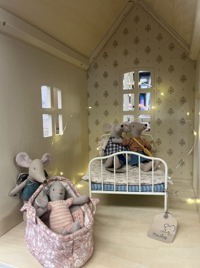 Three stuffed mice are sitting on a bed in a doll house.