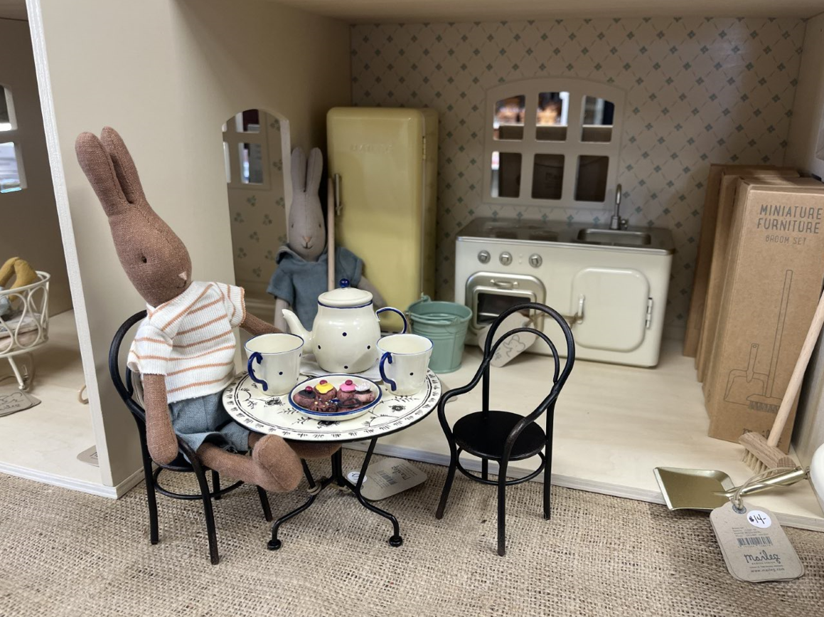 A stuffed rabbit is sitting at a table in a doll house.