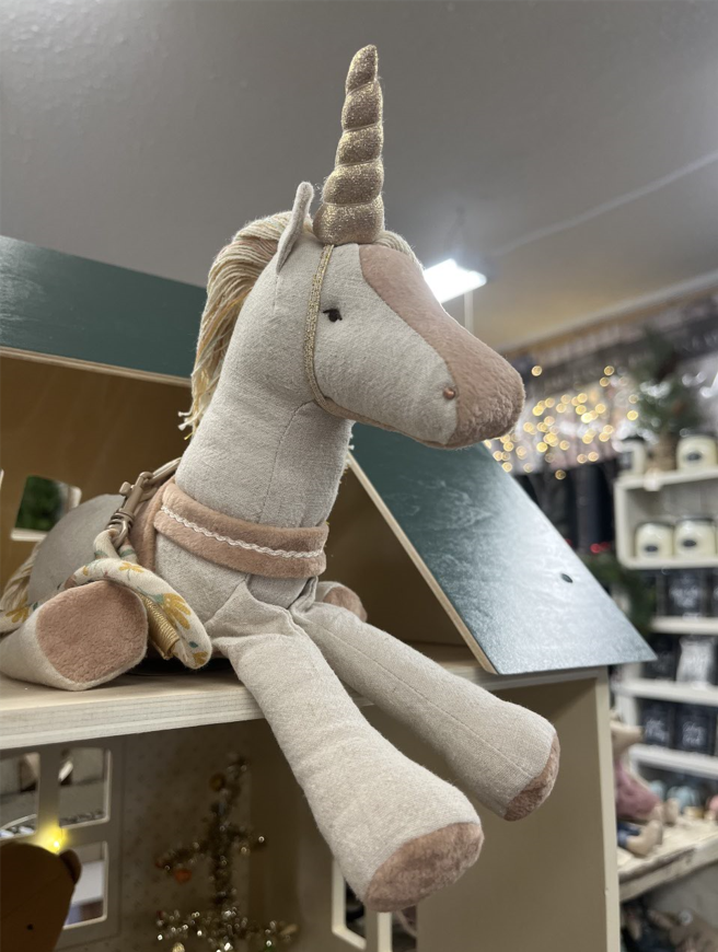 A stuffed unicorn is sitting on a shelf in a store.