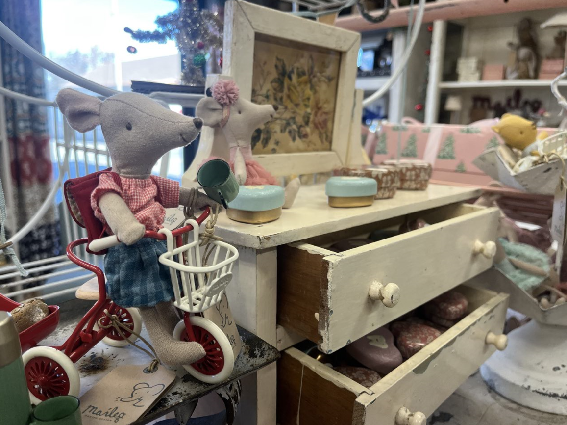 A stuffed mouse is riding a tricycle next to a dresser.