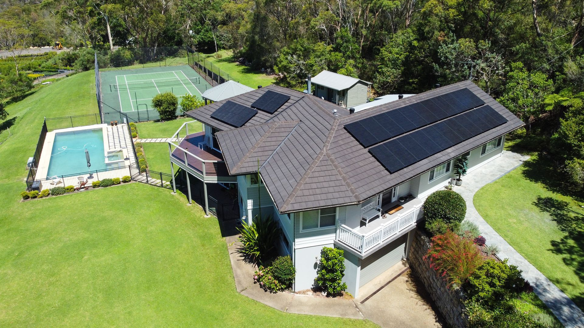 Aerial view of a house with solar panels, backyard pool, and large green lawn