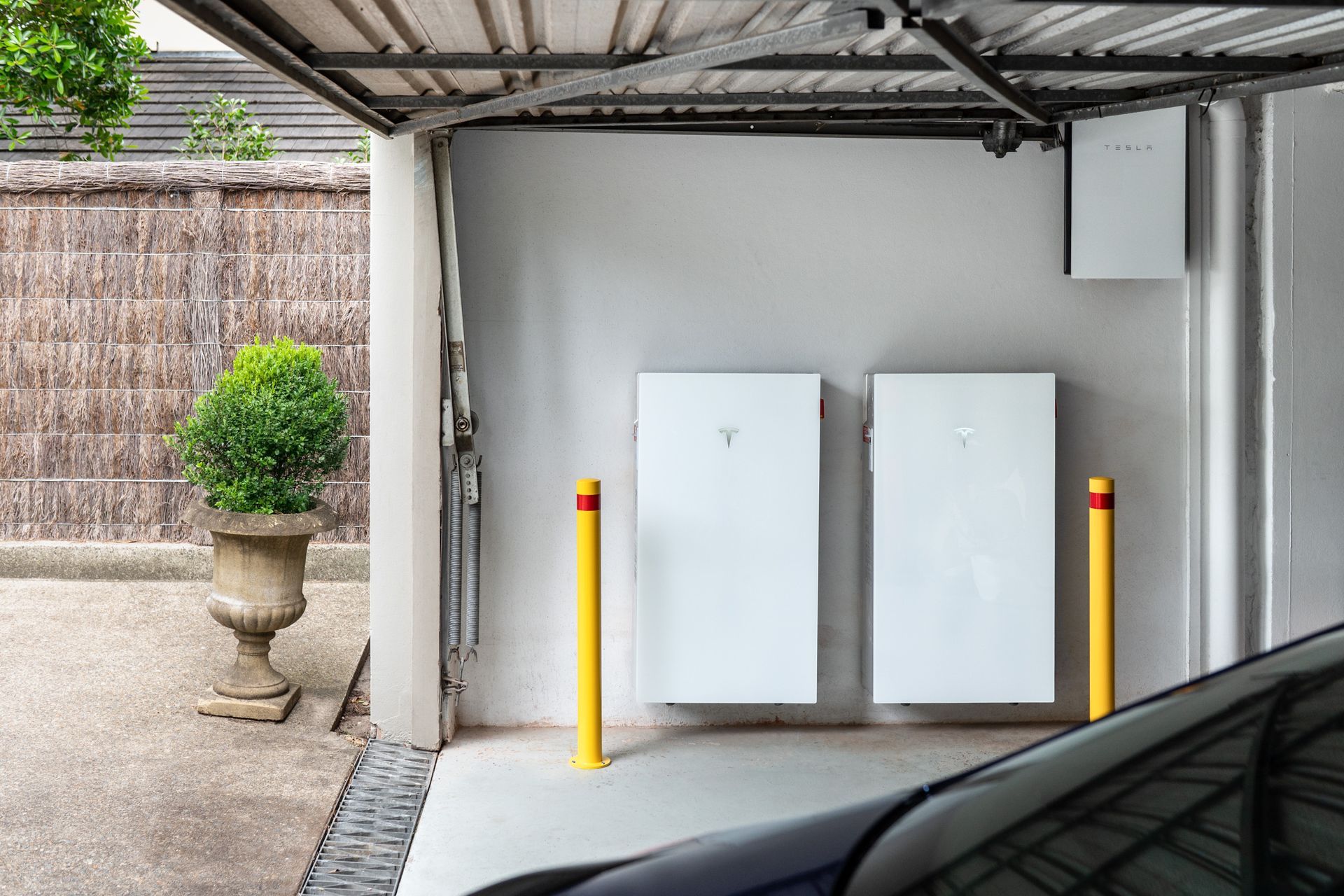 Covered parking area with two white utility boxes and yellow bollards beside a car
