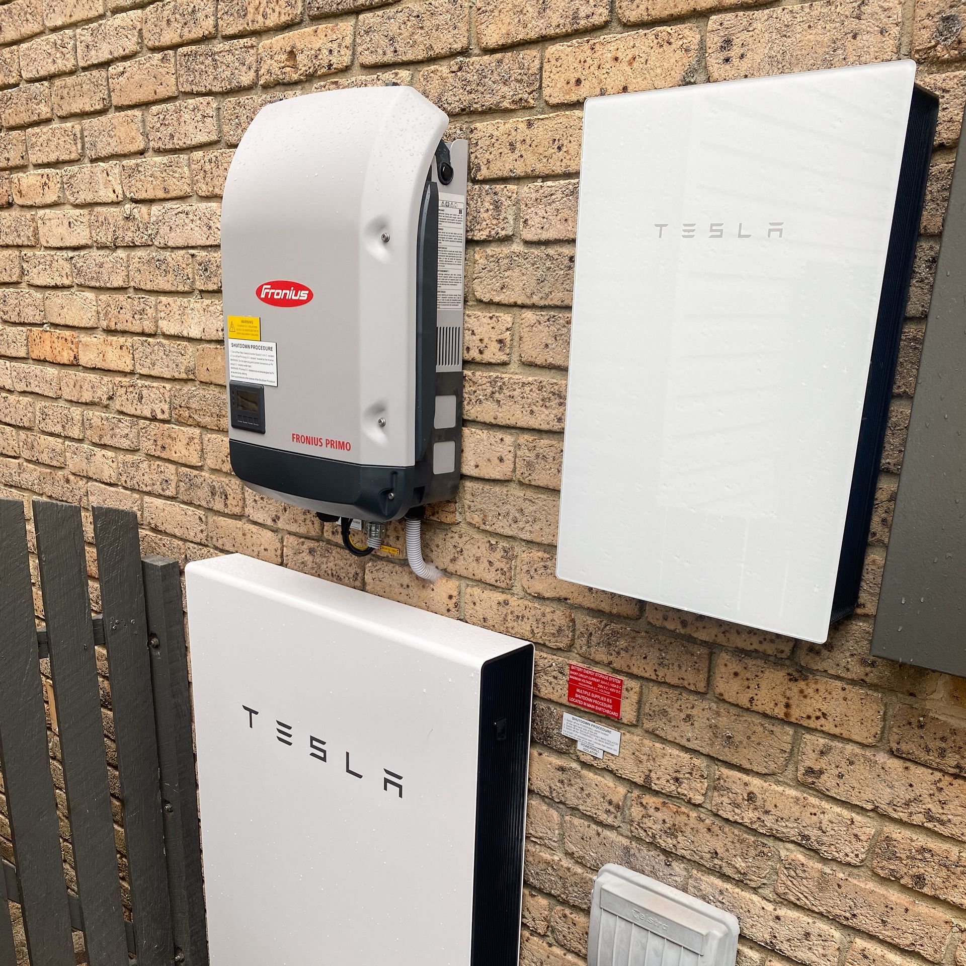 Tesla powerwall units mounted on a brick wall beside a gray utility box