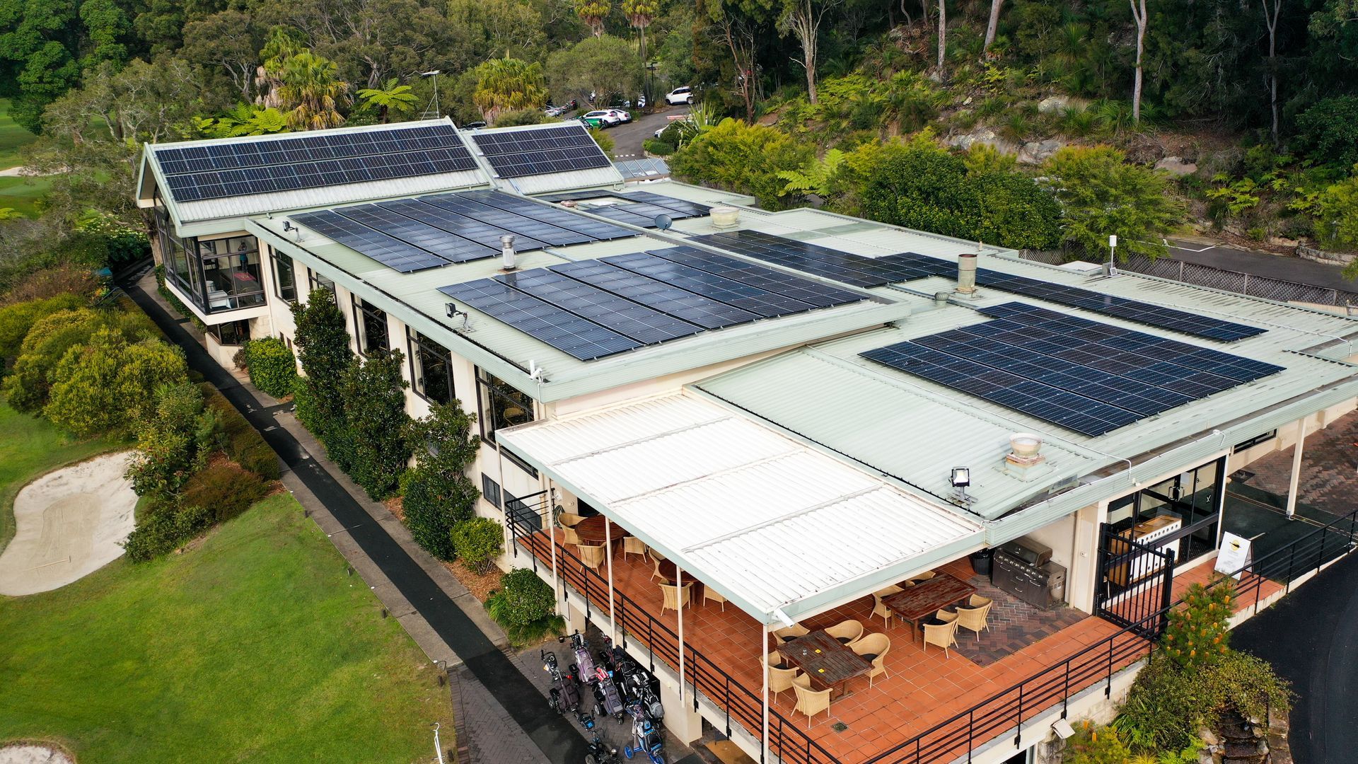 Aerial view of a building with solar panels on the roof, surrounded by trees and greenery.