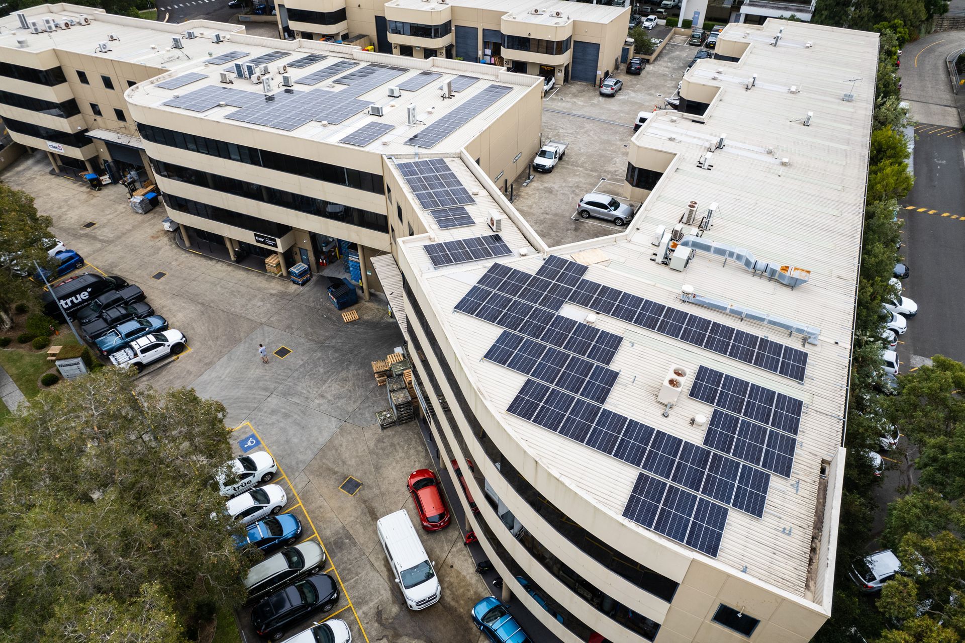 Aerial view of office buildings with large rooftop solar panel arrays and parked cars below