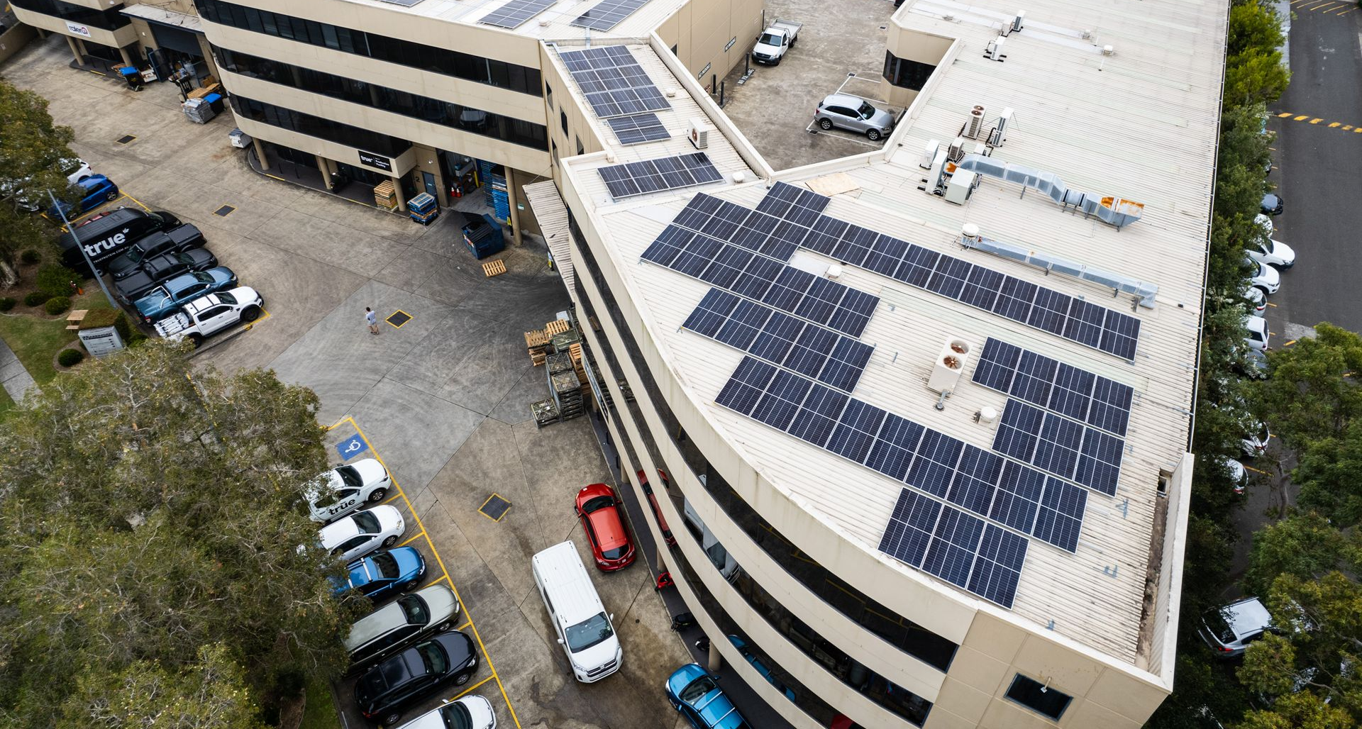 Aerial view of a parking garage rooftop covered with solar panels and surrounding parked cars.