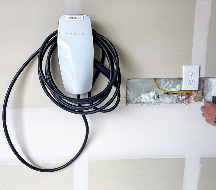 Wall-mounted EV charger with coiled black cable beside a white outlet on a garage wall