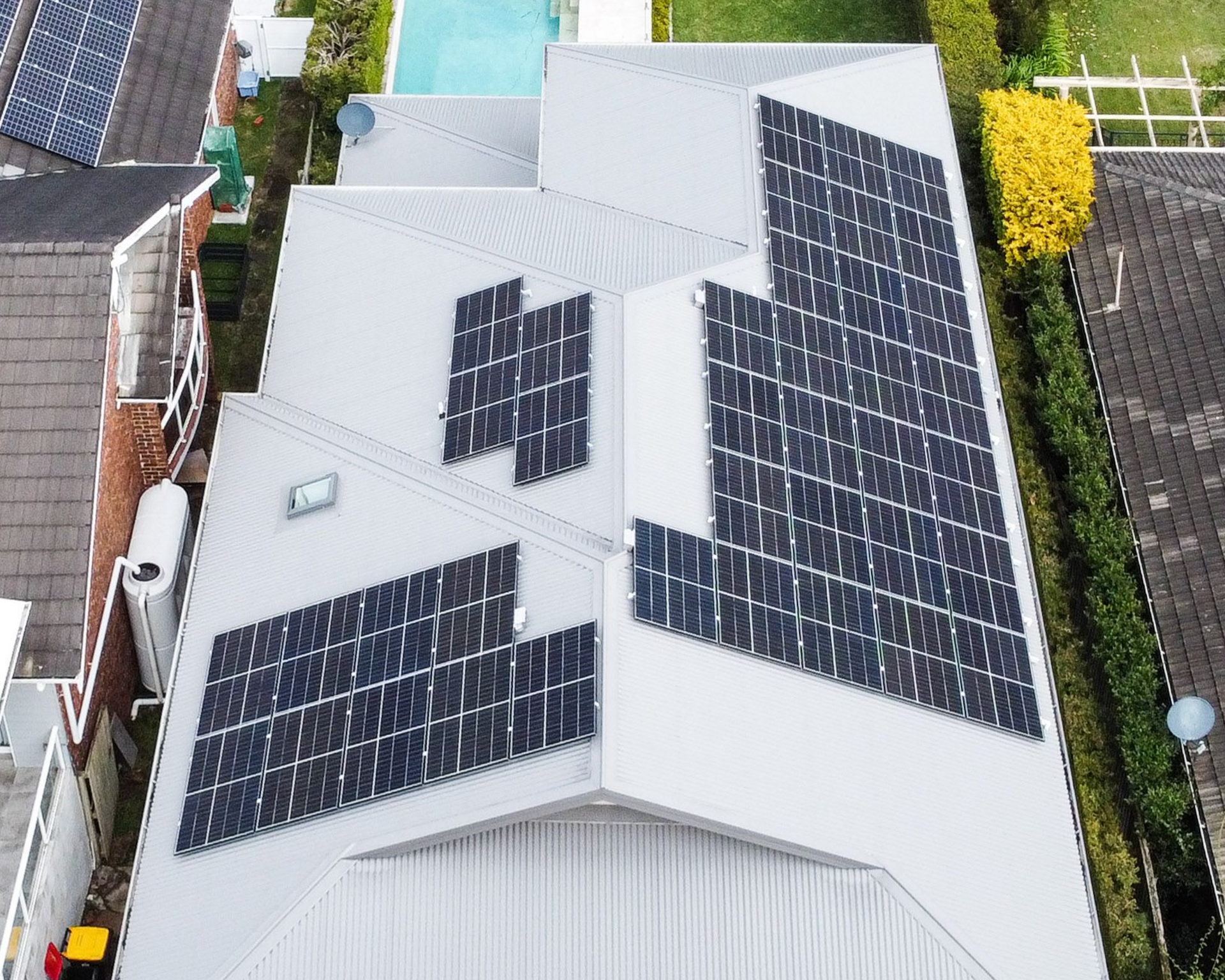 Aerial view of a house roof with multiple black solar panels on light gray metal roofing.