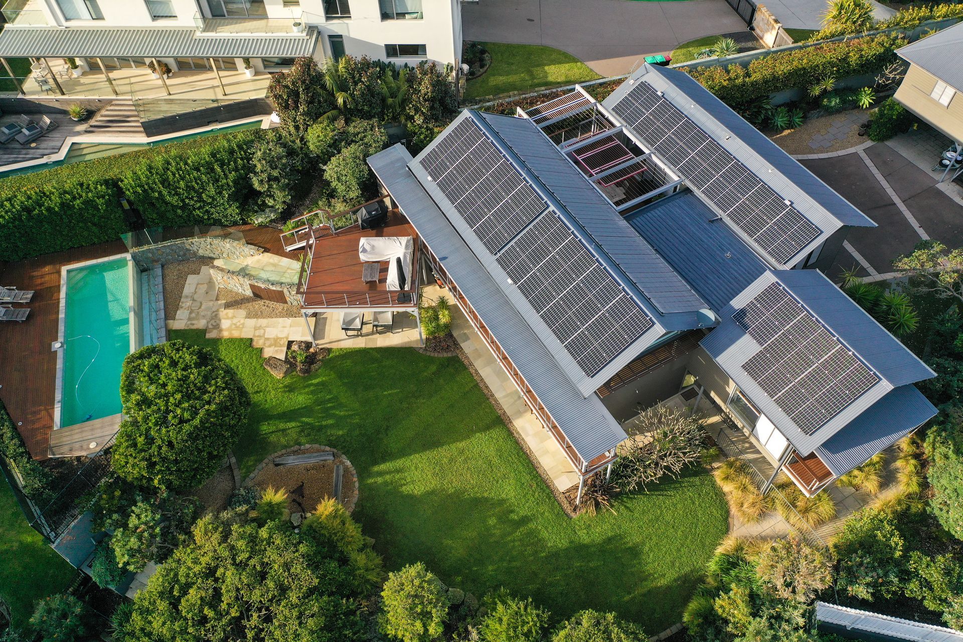 Aerial view of a house with solar panels, green lawn, and a swimming pool in the yard