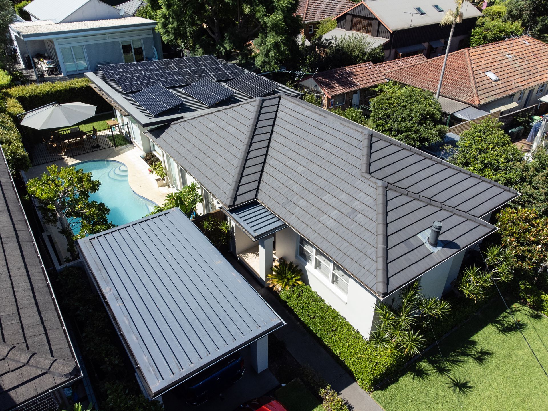 Aerial view of a suburban home with a gray roof, solar panels, pool, and green yard