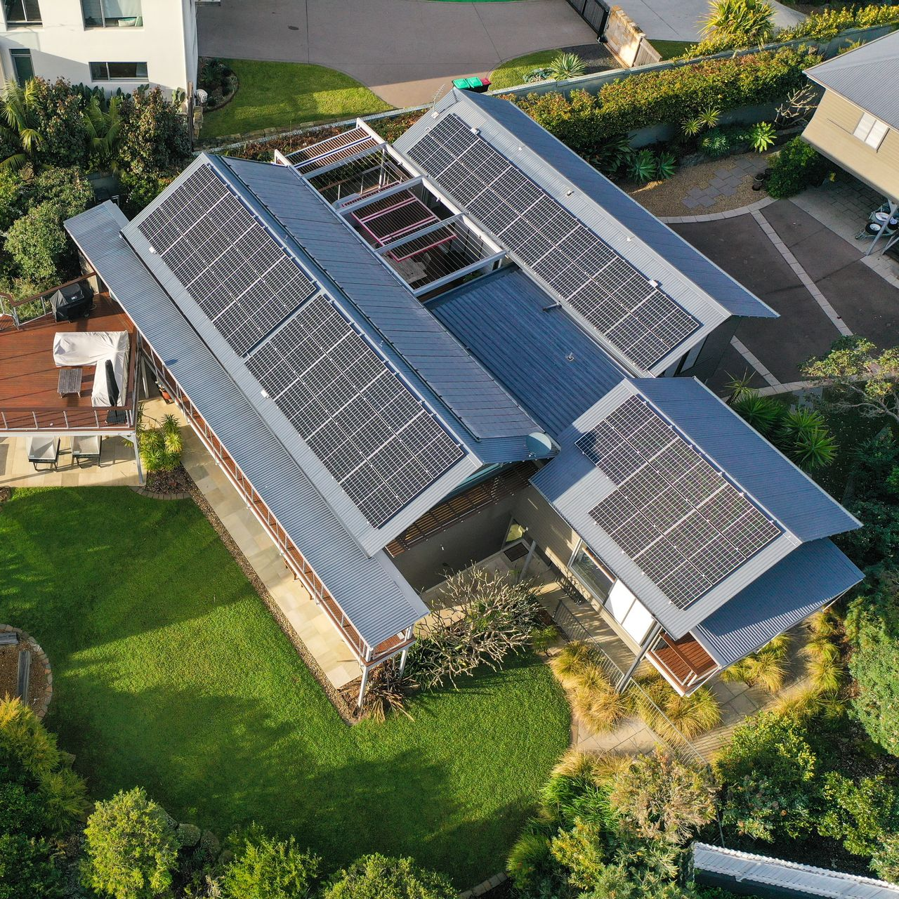 Aerial view of a house with multiple solar panel roofs and a green lawn