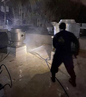 Person pressure washing rooftop vents at night.