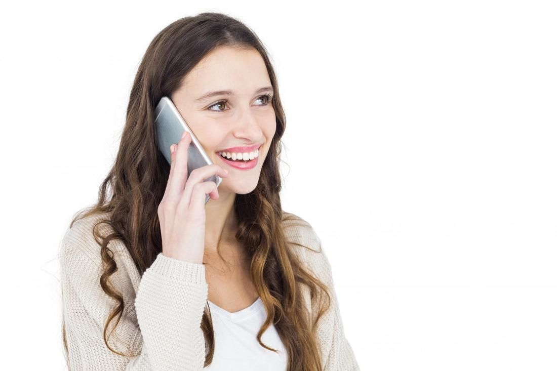 Woman smiling while talking on a smartphone, looking off to the side, wearing a beige cardigan.