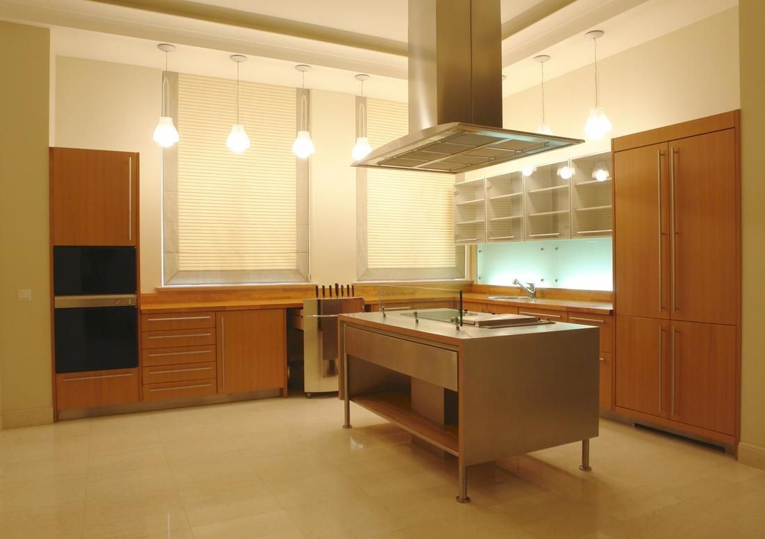 Modern kitchen with stainless steel island, wood cabinets, and pendant lights.