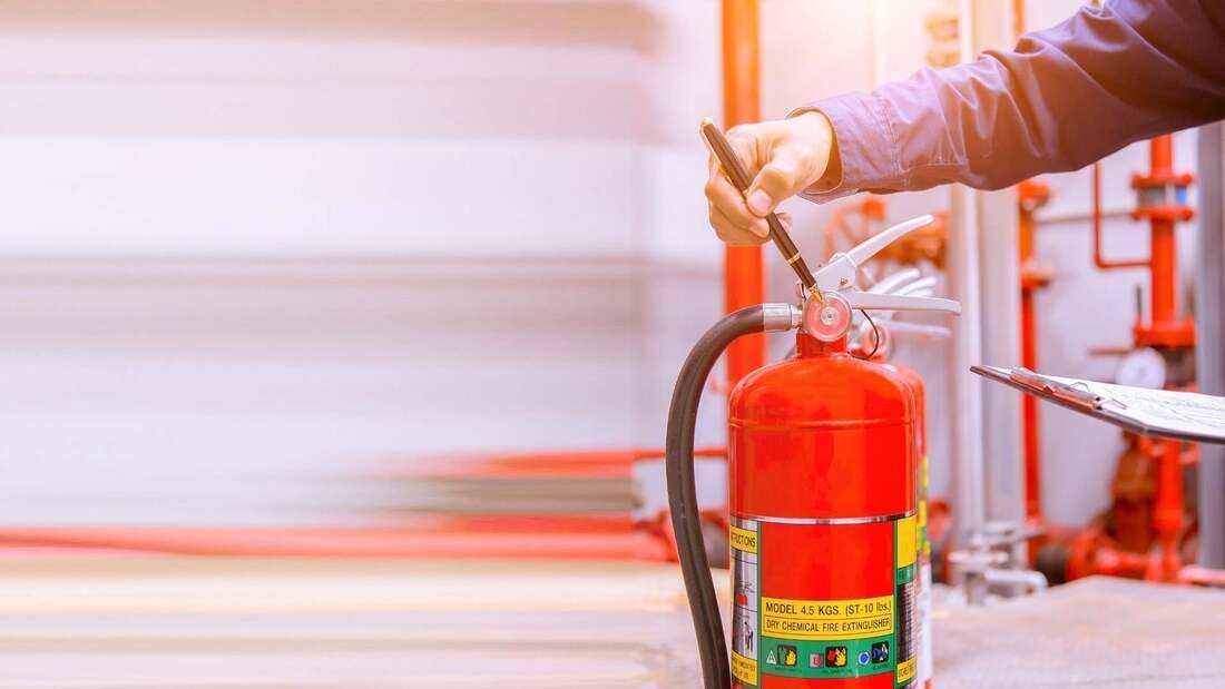 Person inspecting a red fire extinguisher with a clipboard in a building.
