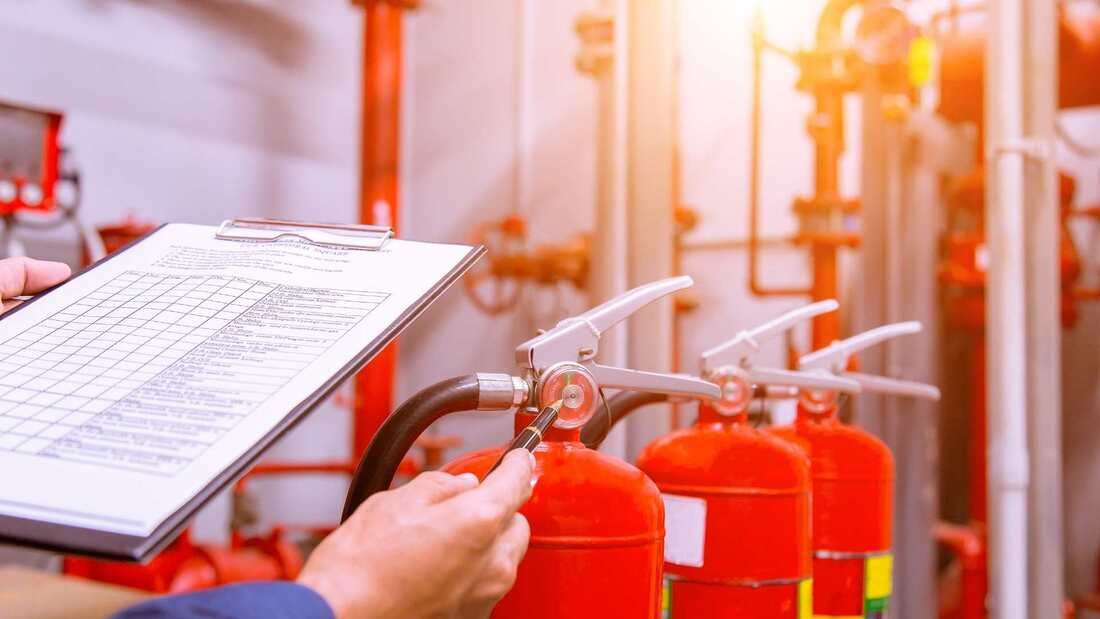Person inspecting fire extinguishers with a clipboard in an industrial setting.