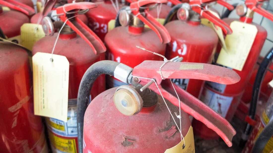 Fire extinguishers, dusty red cylinders with pull pins and hanging tags.