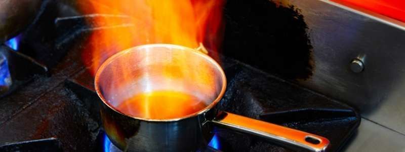 A small pot on a gas stove with flames rising from it.