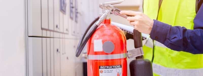 Person in safety vest inspecting a red fire extinguisher.